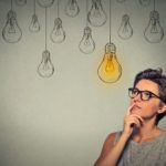 Portrait thinking woman in glasses looking up with light idea bulb above head
