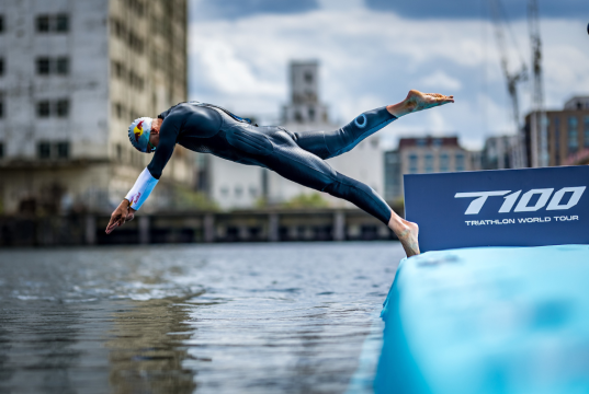 UK exhibitions sector delivered £11.7 billion economic boost in 2025 Triathlete in a wetsuit diving from a blue ramp into the water at a race start, with a T100 Triathlon World Tour banner nearby.
