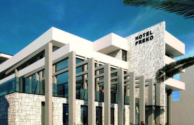 Modern white hotel with stone accent wall and large glass windows under a blue sky; sign reads HOTEL PREKO