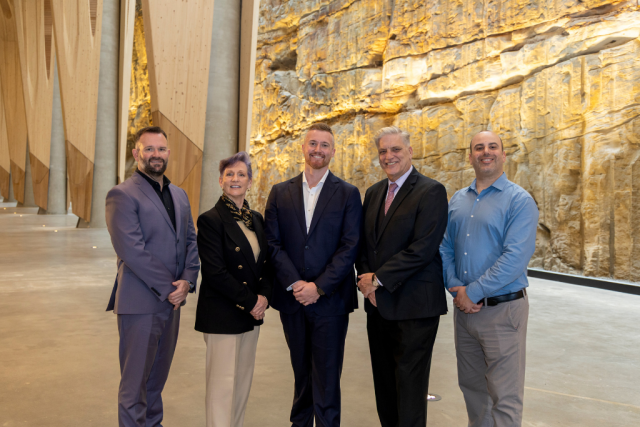 Five professionals posing for a group photo in a bright, modern interior with a rock wall backdrop.