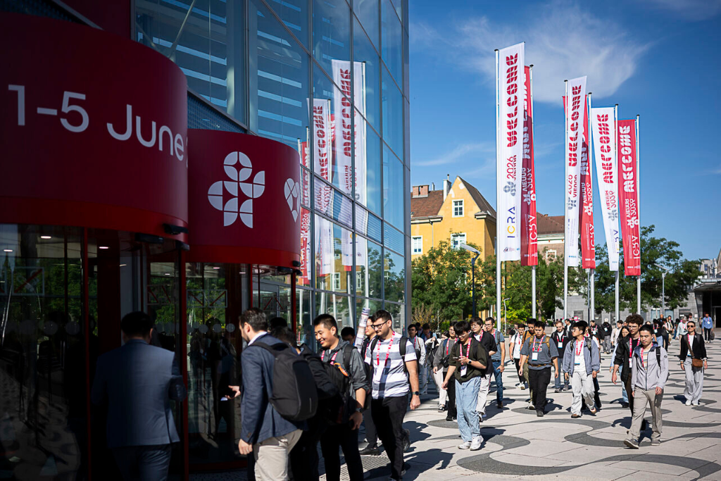 icra_congress People queueing to enter a modern glass building for a conference, with red signage and tall banners outside.
