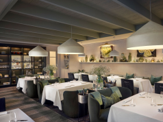 MICHELIN Guide New Zealand 2026 debuts with 110 establishments Elegant restaurant dining room with white-tablecloth tables, green upholstered chairs, and large pendant lights, creating a warm, upscale ambiance.
