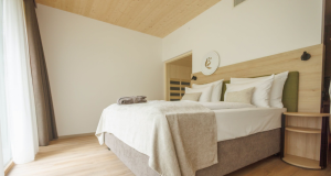 Bright hotel bedroom with a king bed, white linens, beige throw, and a curved wood nightstand by the headboard.