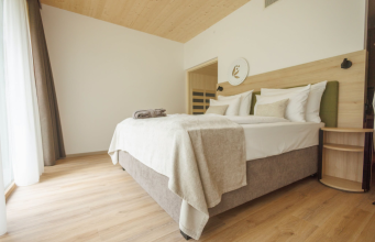 Bright hotel bedroom with a king bed, white linens, beige throw, and a curved wood nightstand by the headboard.