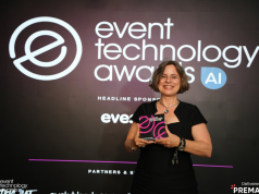 Smiling woman in a black dress on stage holds a pink-and-black award against a dark backdrop that reads 'event technology awards'.