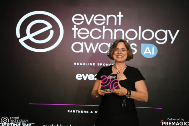 vok_dams Smiling woman in a black dress on stage holds a pink-and-black award against a dark backdrop that reads 'event technology awards'.