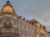 Elegant neoclassical hotel facade at dusk with illuminated 'CORINTHIA' signs on domed towers and ornate balconies