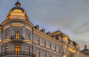 Elegant neoclassical hotel facade at dusk with illuminated 'CORINTHIA' signs on domed towers and ornate balconies